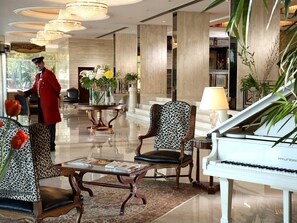 Un lobby imponente con un piano, sillones estampados, una recepción y una gran lámpara de araña.