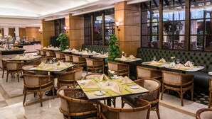 A hotel dining area with multiple tables set for guests, featuring wicker chairs and a green upholstered bench. - Sonesta Hotel Tower & Casino Cairo (Cairo)