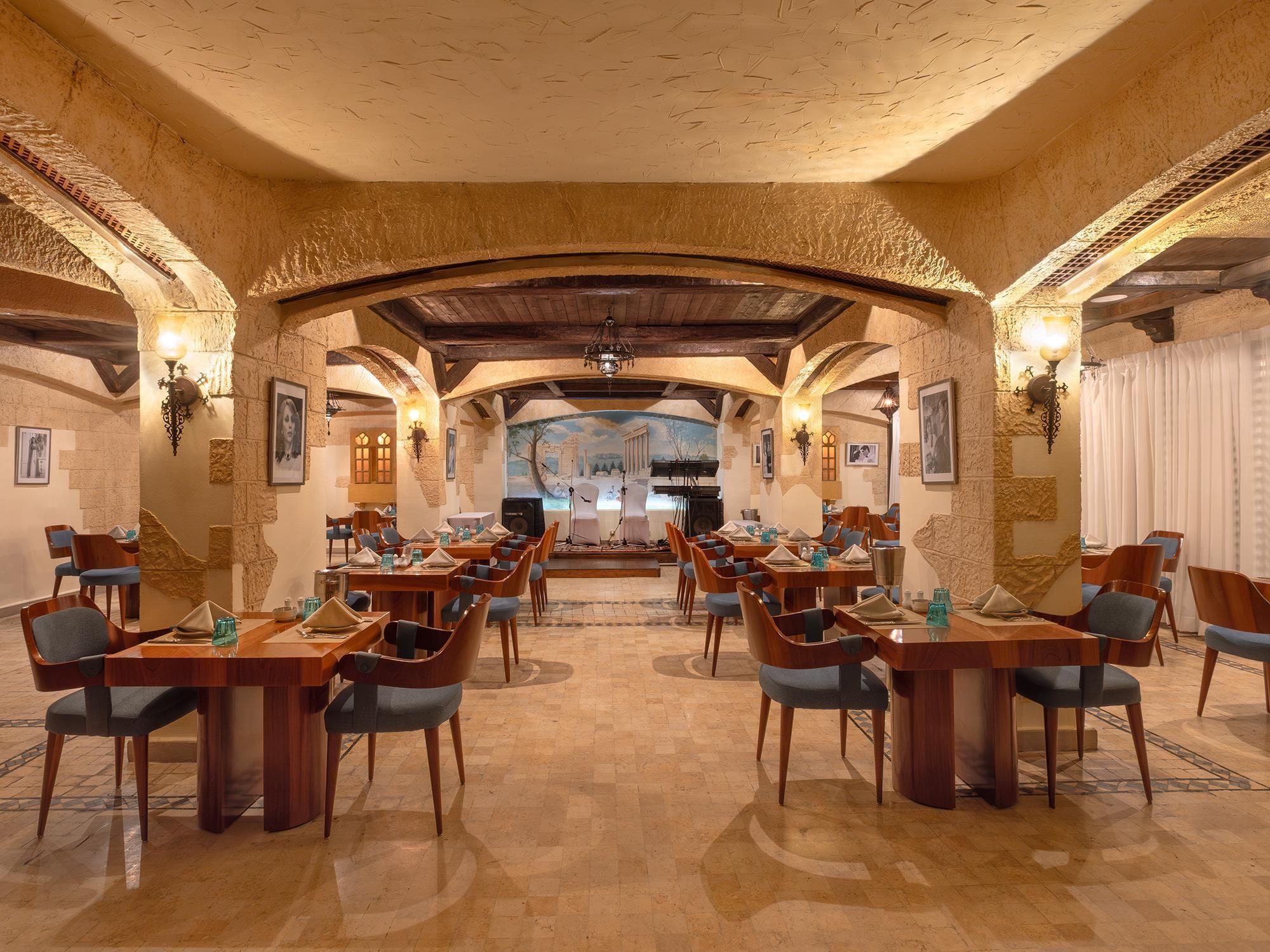Un comedor amplio con varias mesas y sillas, paredes de piedra y un mural en la pared de fondo.