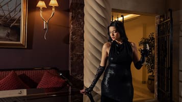 A woman in a black dress standing in a room with a red sofa, a painting, and a lamp.