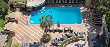 Un área de piscina con sillones de descanso, una palmera y un deck empedrado.