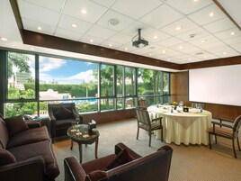 Un salón de conferencias con una amplia mesa, sillas, un proyector y vistas a una piscina y edificios.