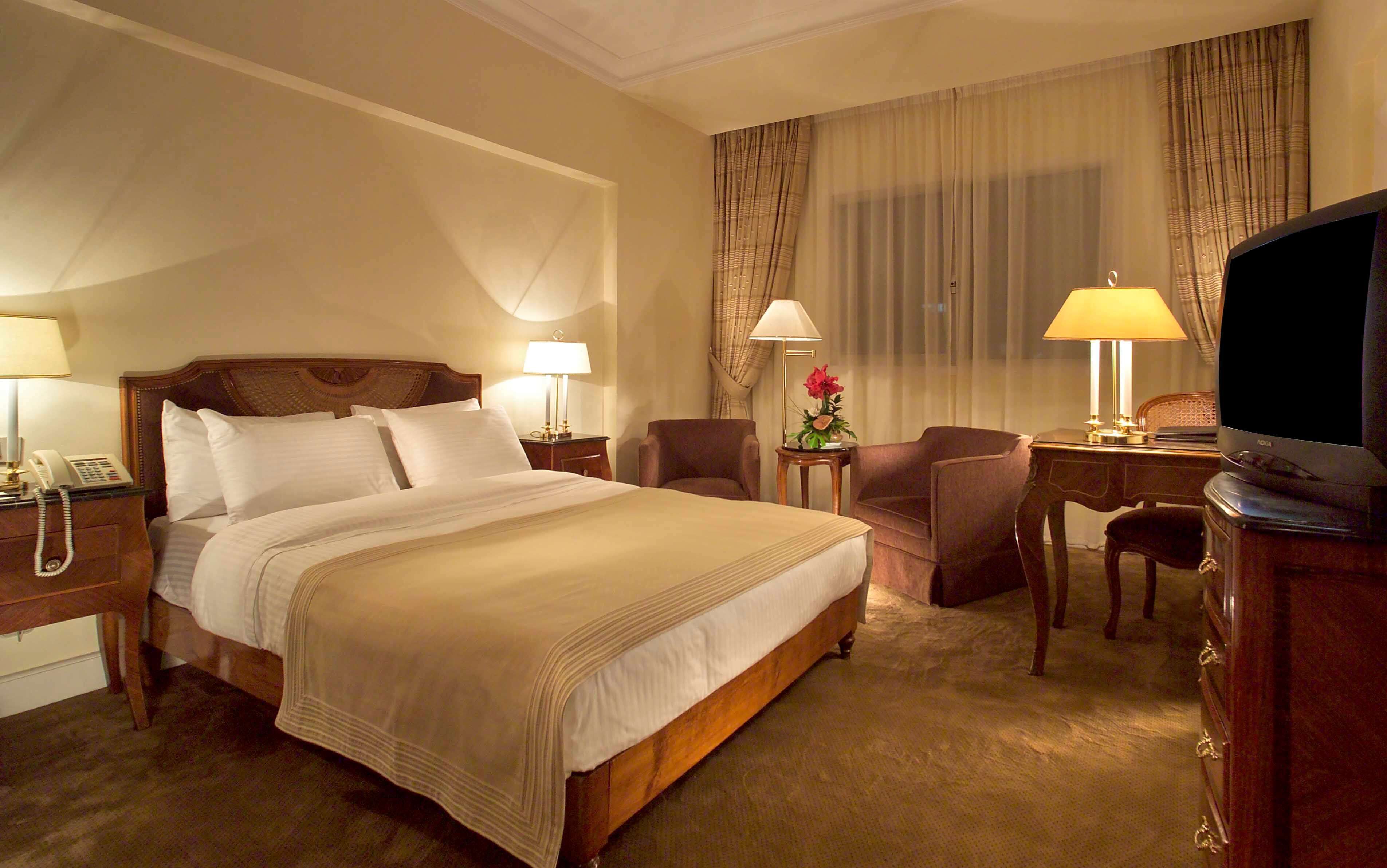 A hotel room with a large bed, two bedside tables with lamps, a desk with a chair, and a television.