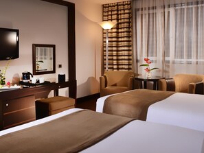 Habitación de hotel con dos camas, un escritorio con cafetera, una silla, televisor y ventana con cortinas.