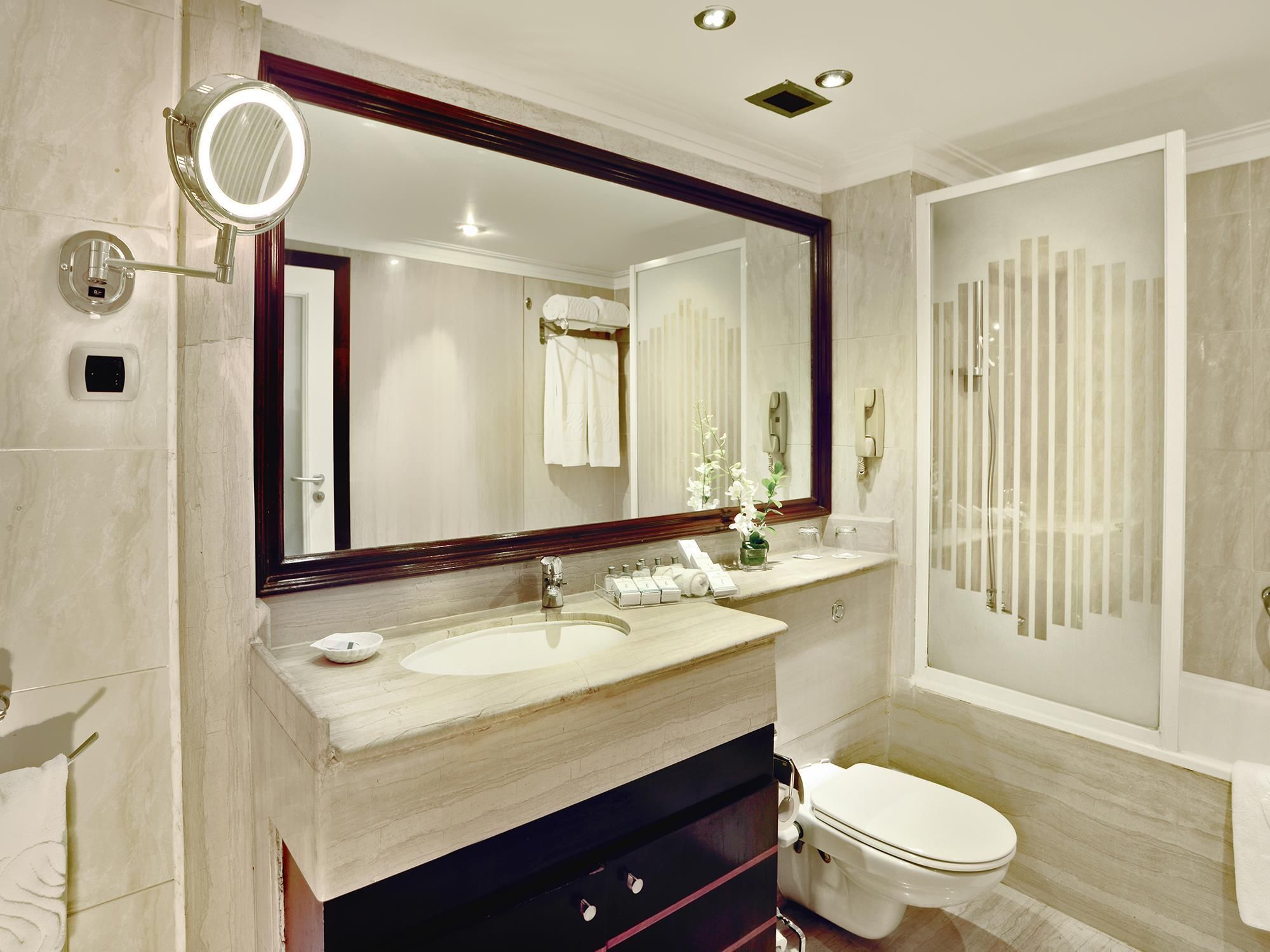 A modern bathroom with a large mirror, a sink, a toilet, and a shower area.