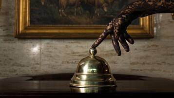A hand reaching towards a bell on a wooden surface, with a framed painting in the background.