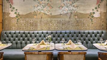 A restaurant with a green upholstered booth seating area, wooden chairs, and a table set with plates, glasses, and cutlery.