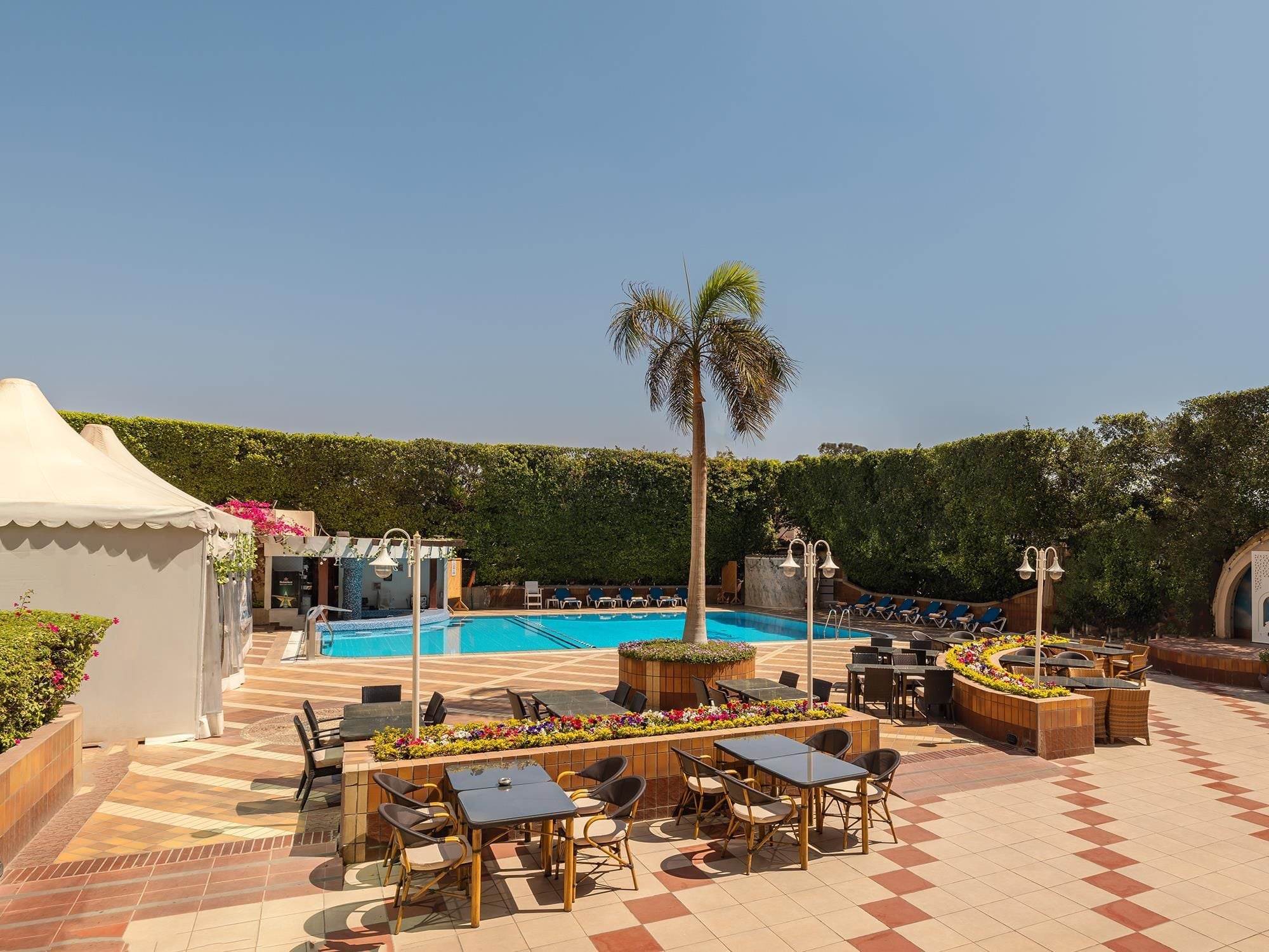 A poolside area with a swimming pool, lounge chairs, and tables.