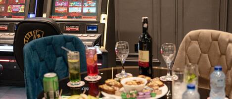 A dining table set with food, drinks, and a bottle of wine, with slot machines in the background.