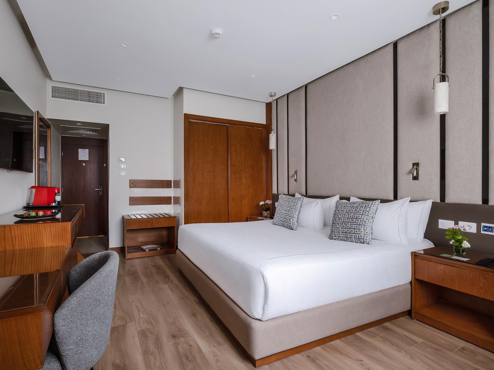 Habitación de hotel con una cama grande, un escritorio con una silla roja, un armario y un espejo.