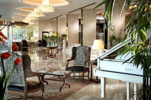 A grand lobby with a white grand piano, leather chairs, and a large chandelier.