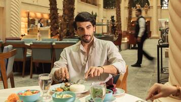 A man dining at a table with various dishes and a waiter in the background.