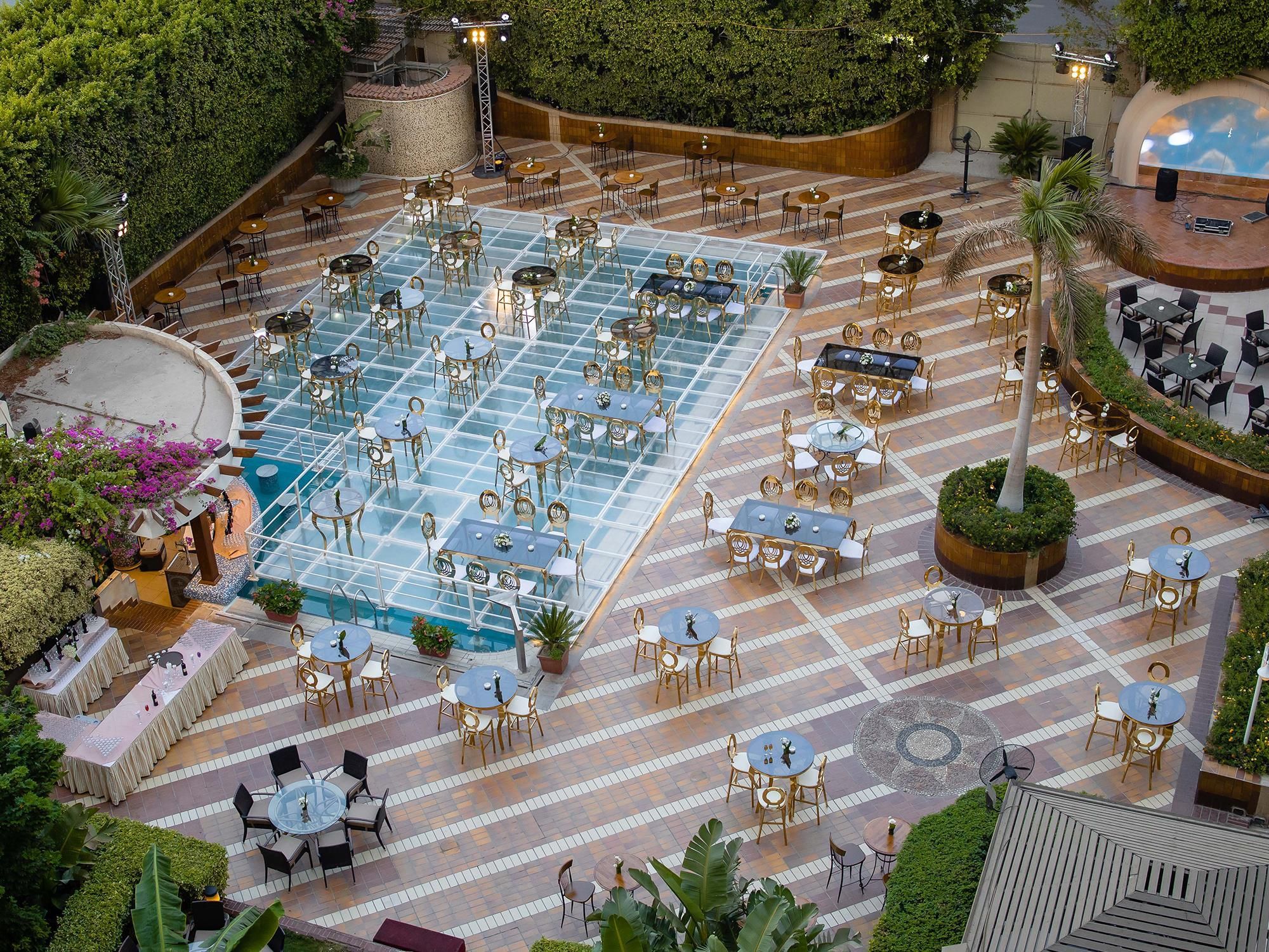 Ein Essbereich im Freien mit mehreren Tischen und Stühlen, umgeben von viel Grün und einem Pool.