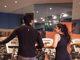 Un hombre y una mujer usando equipo de ejercicio en un gimnasio con un muro espejado.