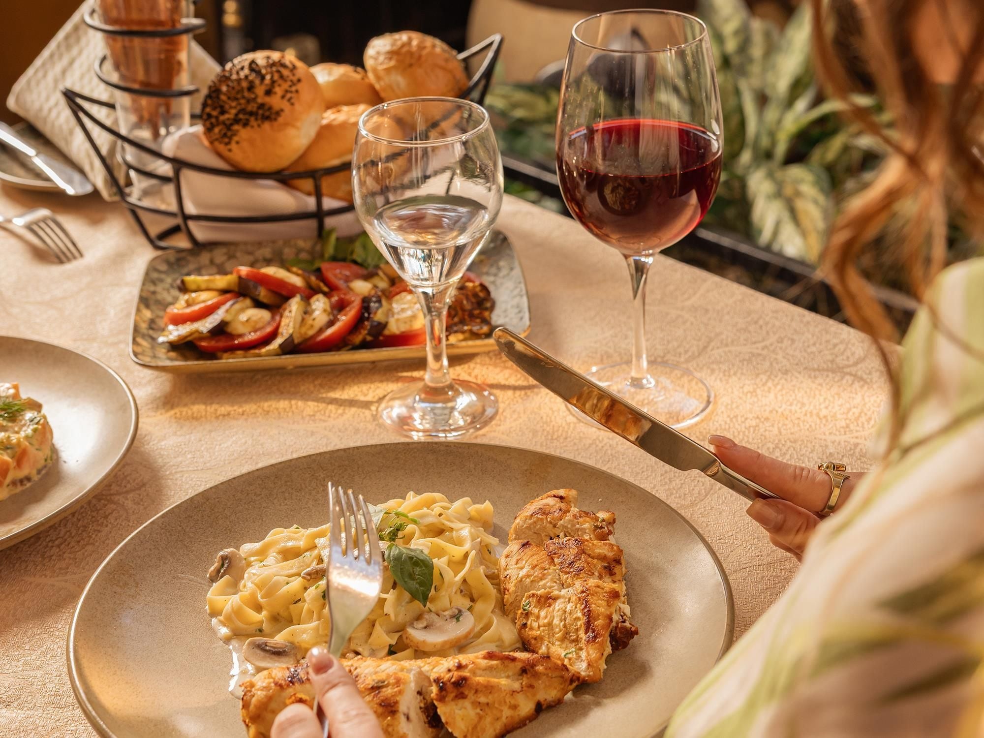 A dining table with a plate of pasta, grilled chicken, and a glass of red wine.