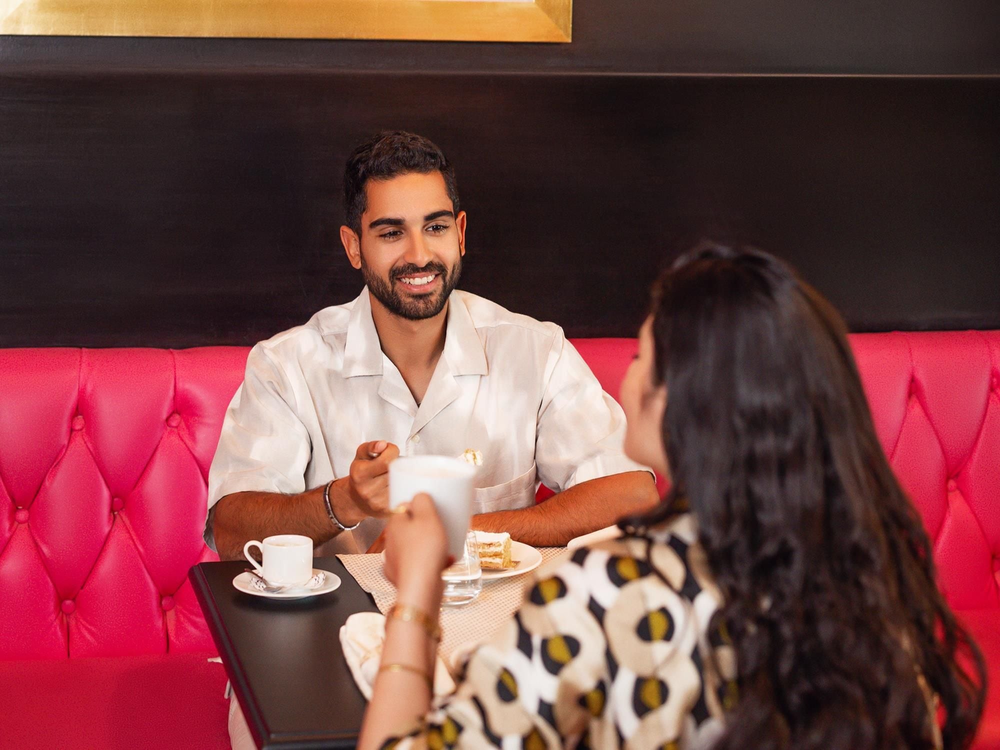 A man and a woman sitting at a table in a room with a red upholstered bench.