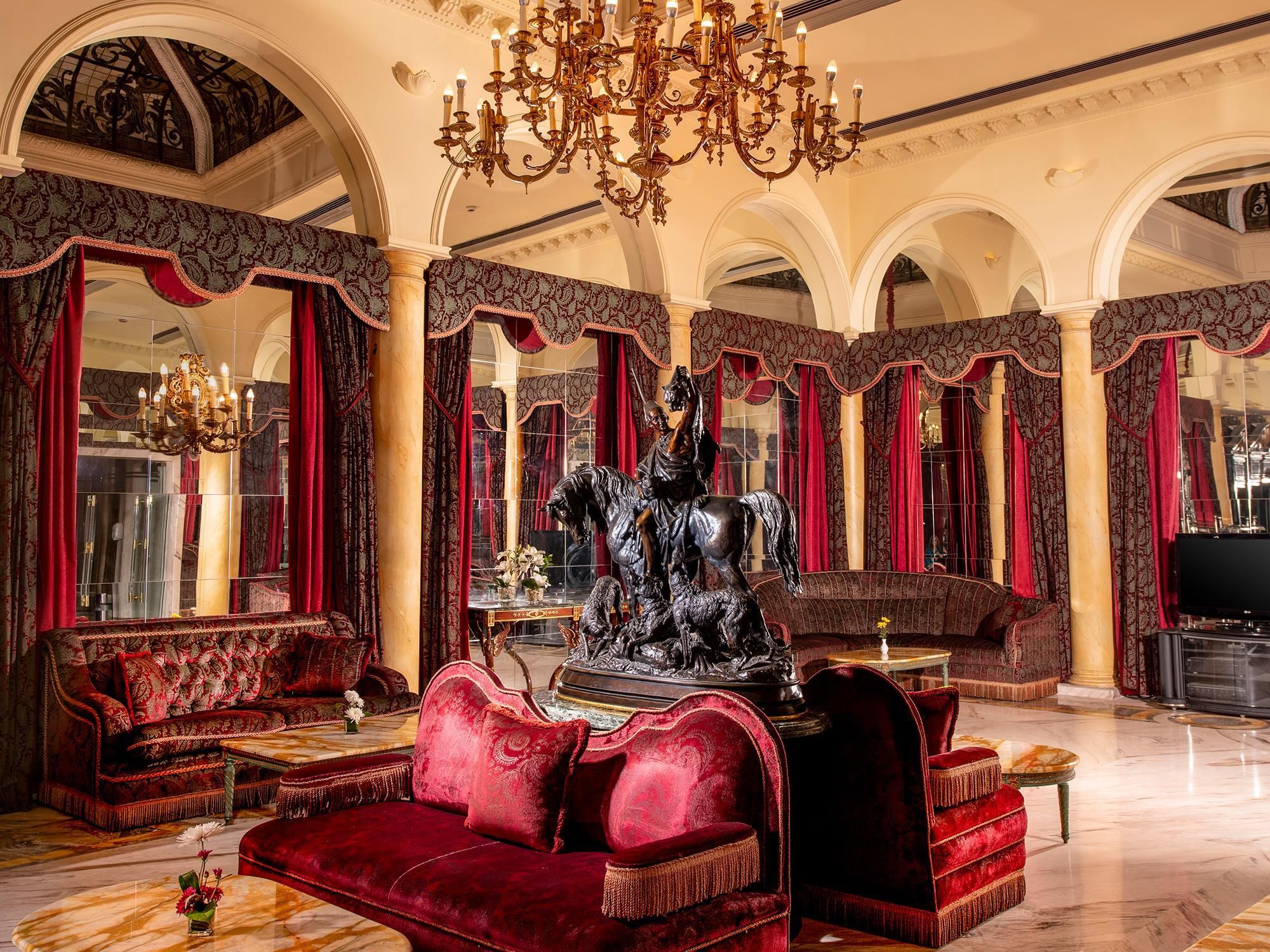 A luxurious interior with a grand chandelier, ornate columns, and plush red sofas.