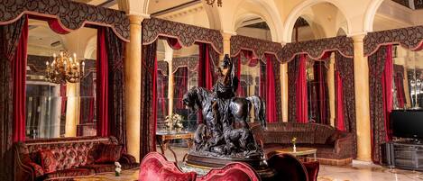 A luxurious interior with a grand chandelier, ornate columns, and plush red sofas.