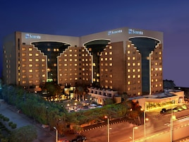 A hotel with multiple floors, a well-lit entrance, and a landscaped area with trees and a pool.