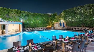 Un'area piscina con poltrone a sdraio e tavoli, una piscina e una zona salotto coperta.
