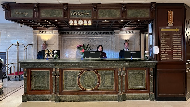 A reception desk with a marble top, two receptionists, a clock, and a sign listing hotel amenities. - Sonesta Hotel Tower & Casino Cairo (Cairo)