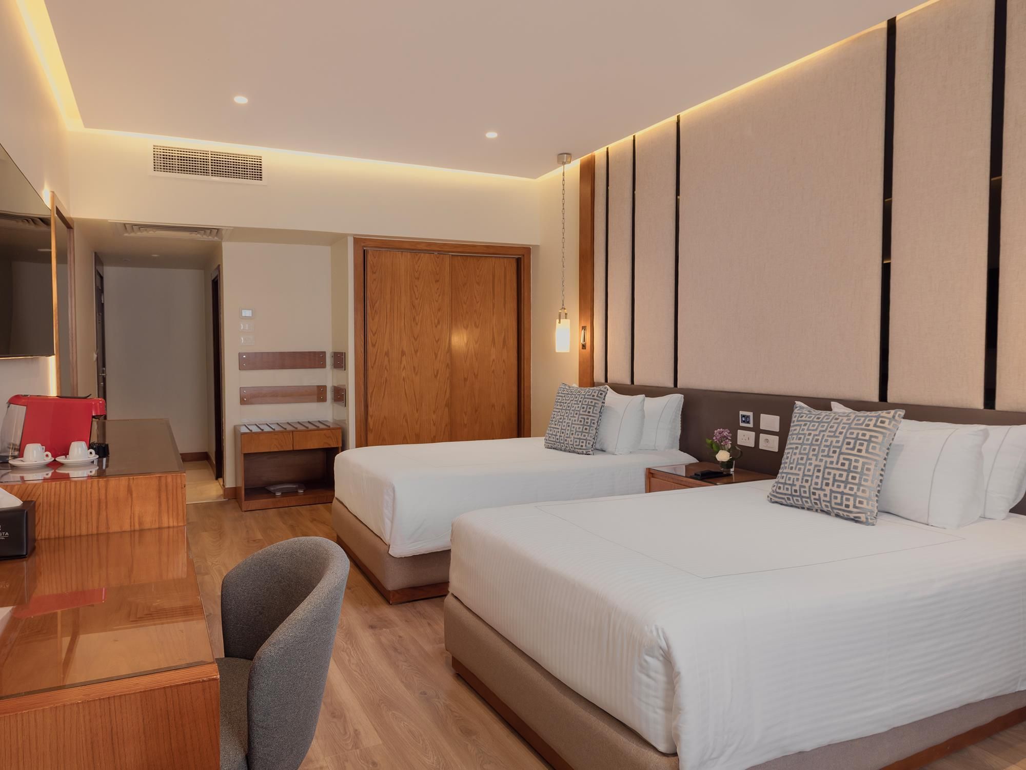 A hotel room with two beds, a desk, a chair, a wardrobe, and a TV.