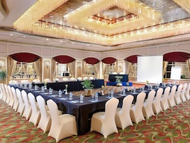 A banquet hall with long tables, white chairs, and a stage for presentations.