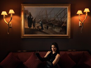A person seated on a red patterned sofa in a room with a framed painting and wall-mounted lamps. - Sonesta Hotel Tower & Casino Cairo (Cairo)