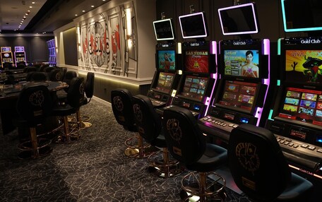 A casino floor with gaming machines, chairs, and a wall with a large logo.