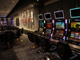 Un salón de casino con máquinas tragamonedas, sillas y una pared con un logotipo grande.