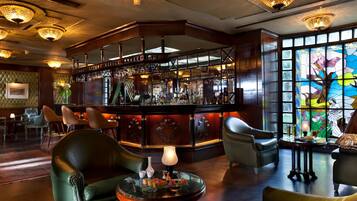 A bar area with leather chairs, a round table with a lamp, and a stained glass window.