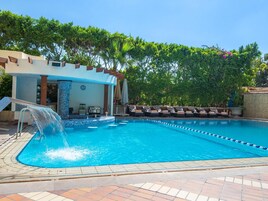 Una piscina con fuente de agua, sillas de descanso y una zona de estar cubierta.