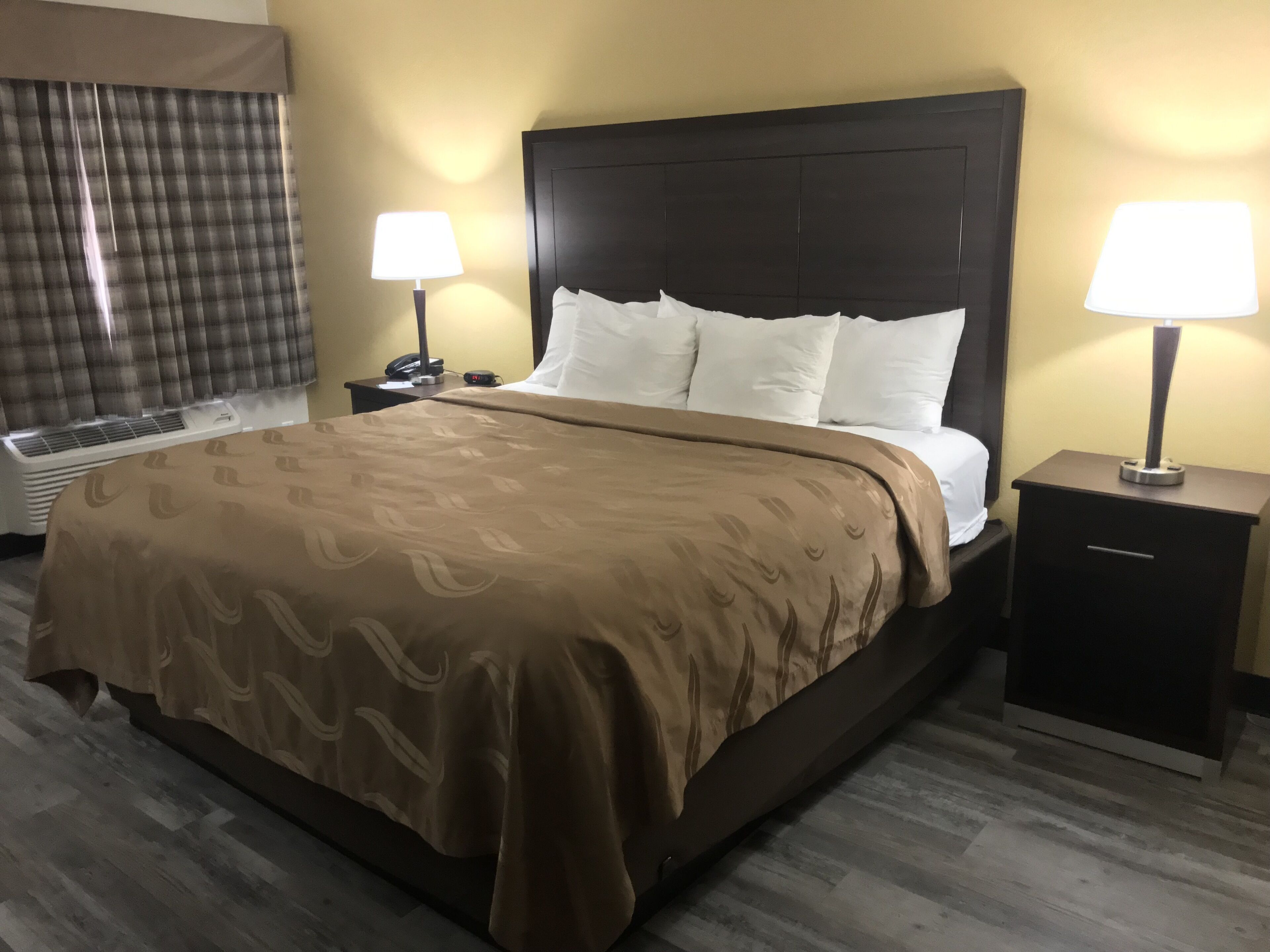 Une chambre d’hôtel avec un grand lit, deux tables de chevet avec des lampes, un radiateur et une fenêtre avec des rideaux.