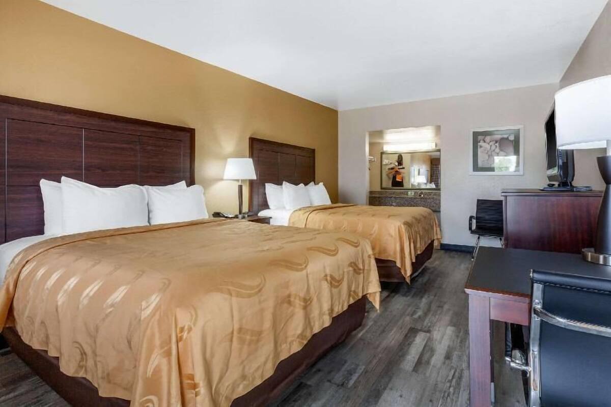 A hotel room with two beds, a desk, a chair, a lamp, and a mirror.