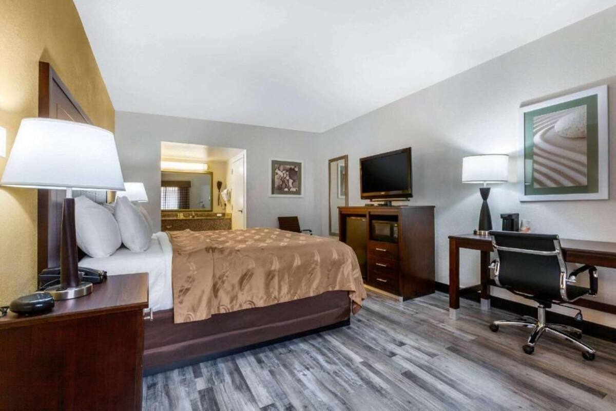 A hotel room with a bed, desk, chair, TV, and artwork on the walls.