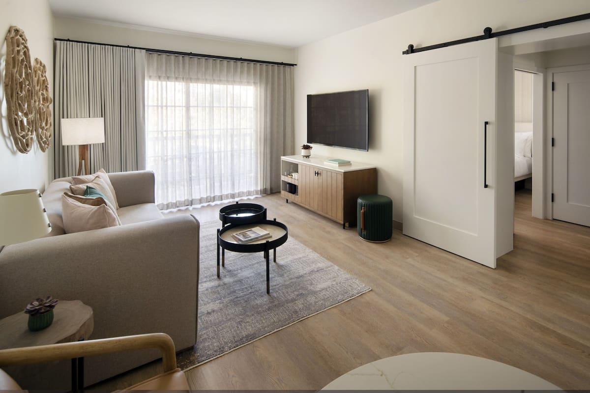 A modern hotel room with a sofa, a coffee table, a TV, a cabinet, and a sliding door.