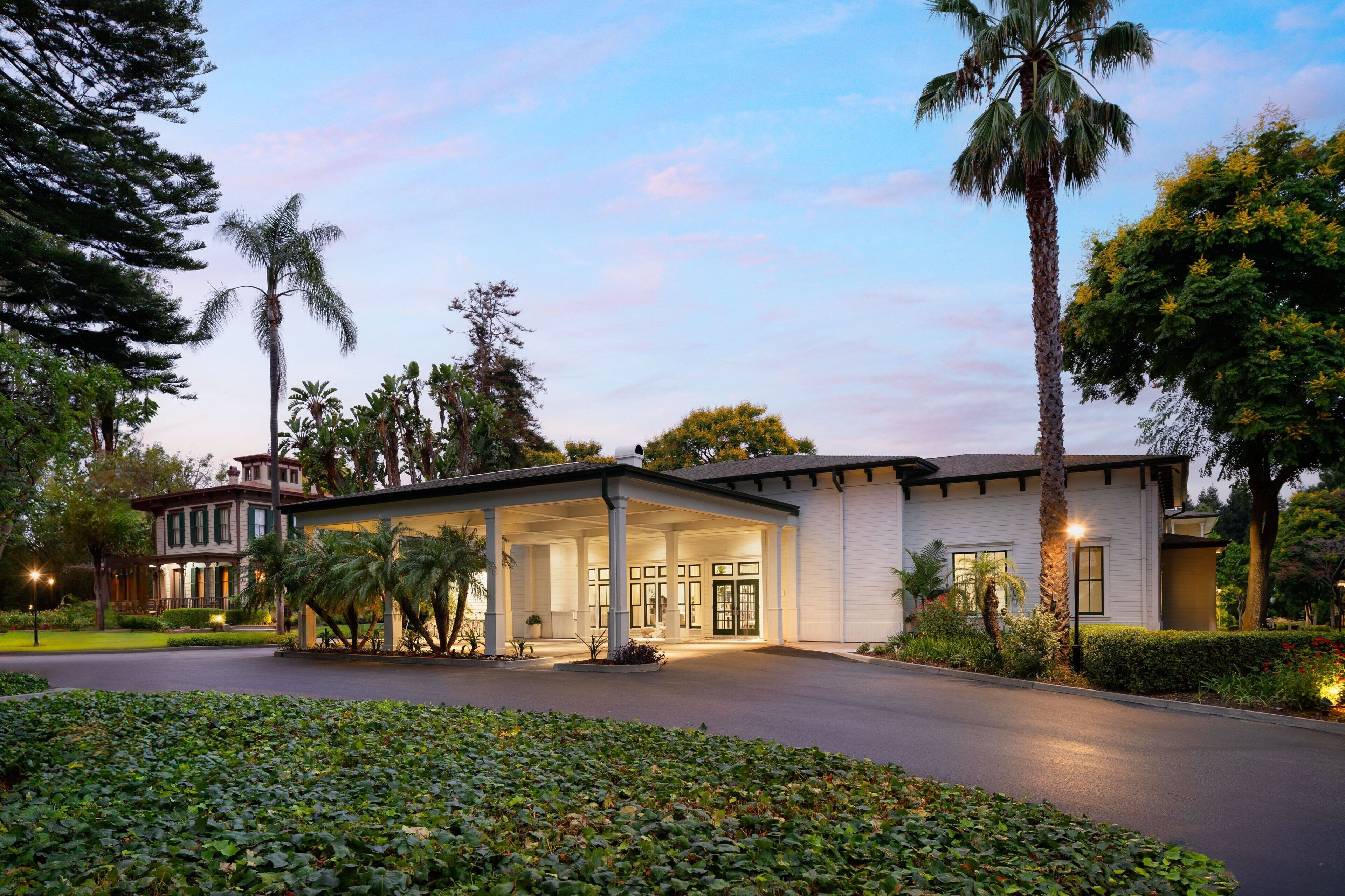 A two-story building with a covered entrance, palm trees, and a well-maintained garden.