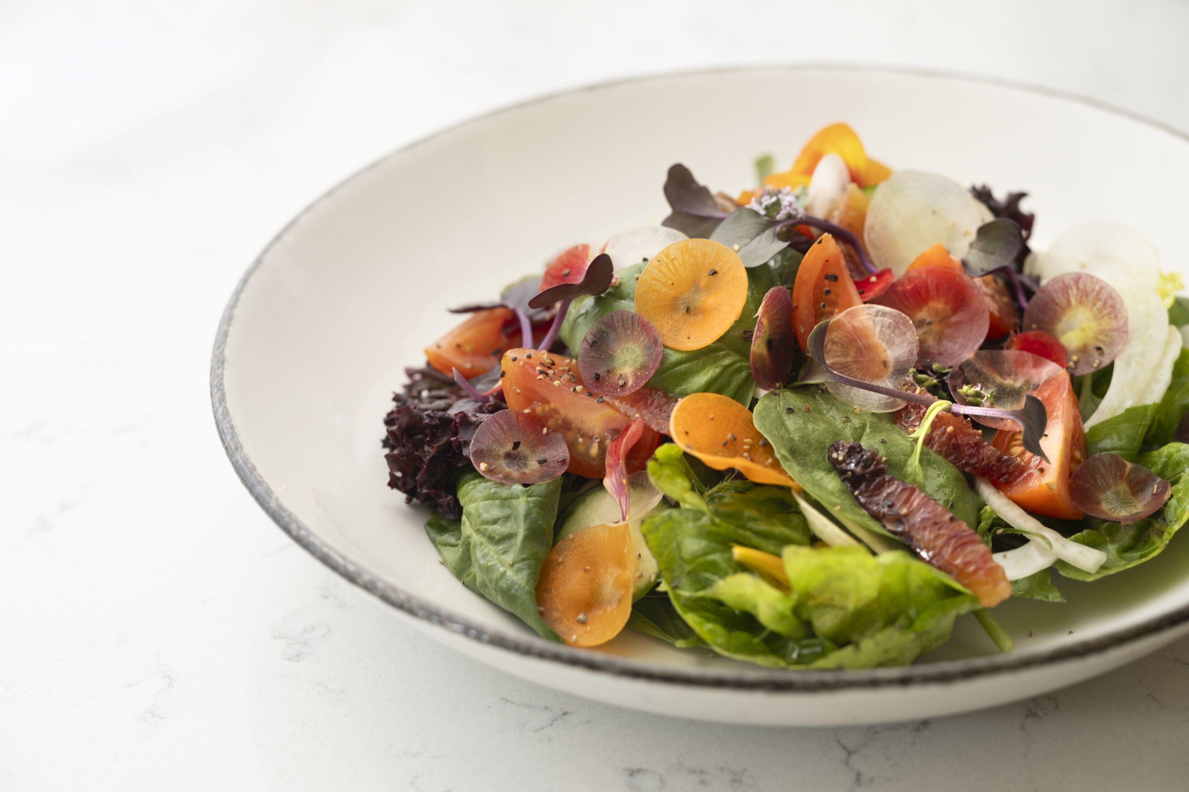 A bowl of salad with various greens and vegetables.