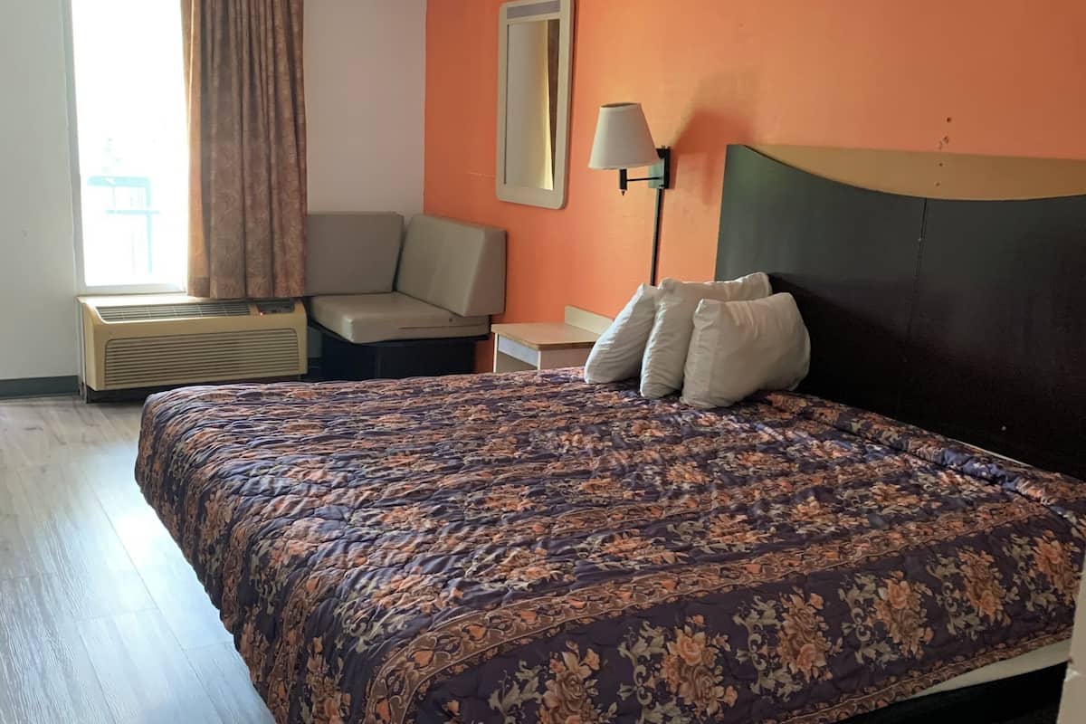 A hotel room with a large bed, a sofa, a small table, a lamp, and a window with curtains.
