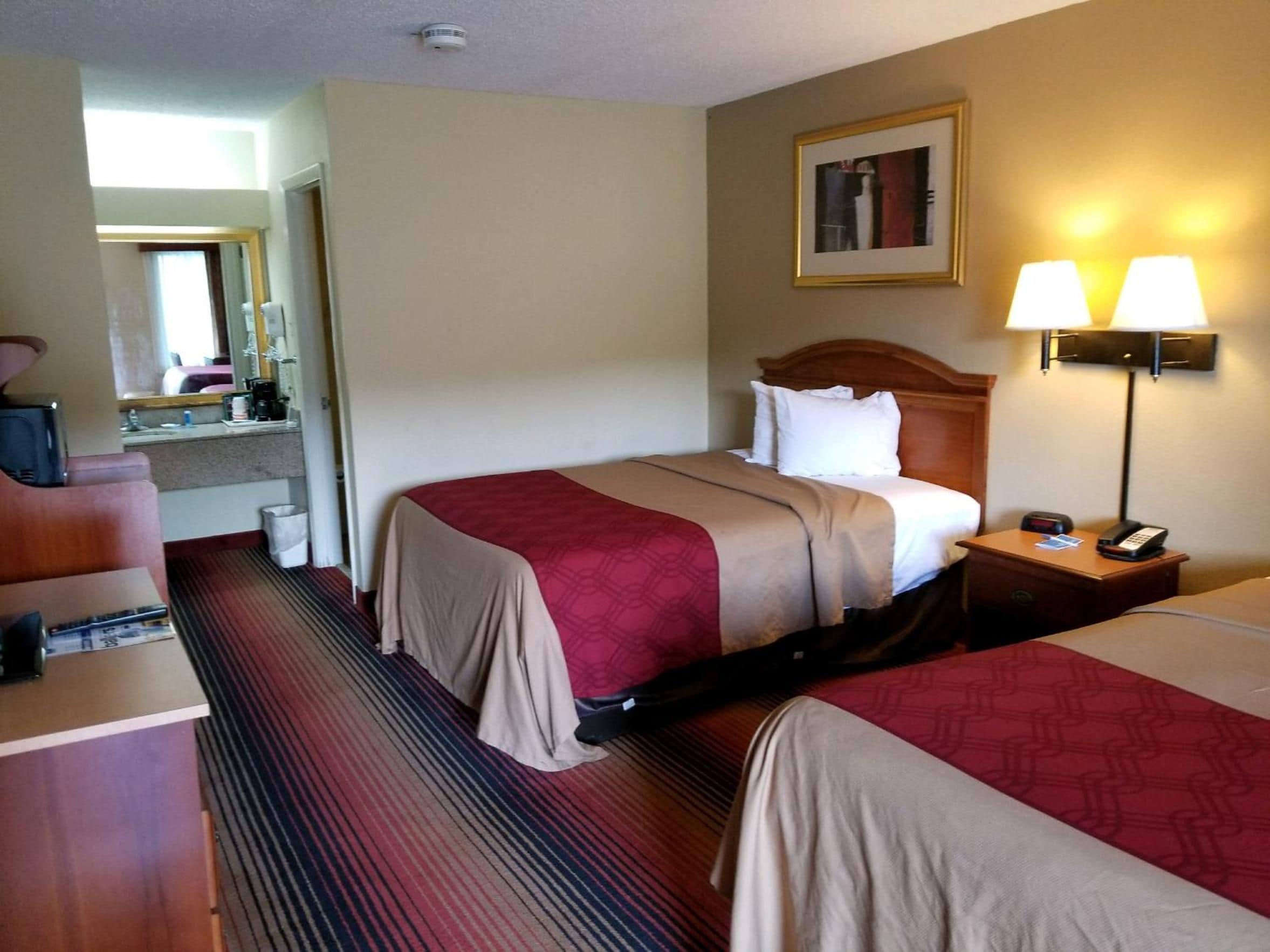 A hotel room with two beds, a desk, a chair, a lamp, and a phone on a bedside table.