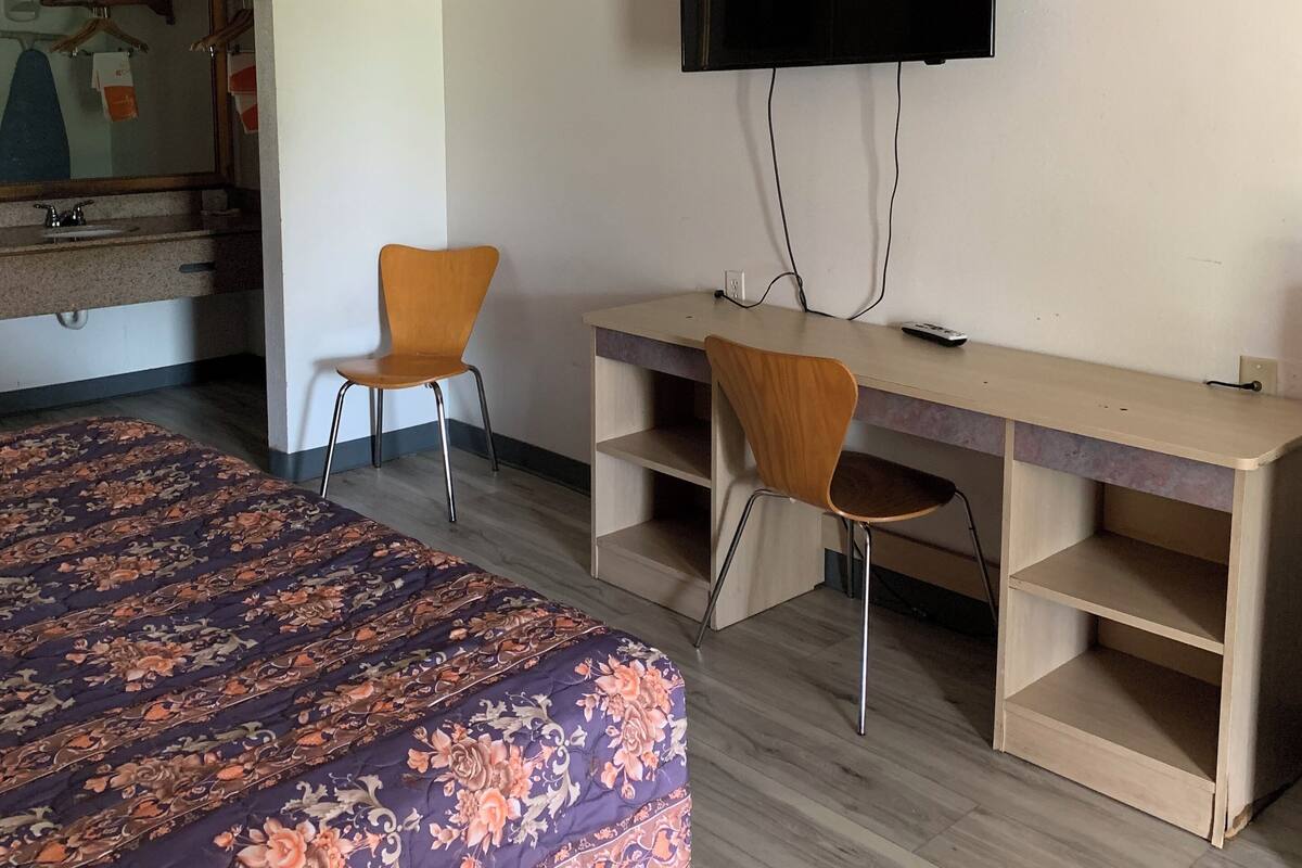 A hotel room with a bed, two chairs, a desk, a television, and a mirror.