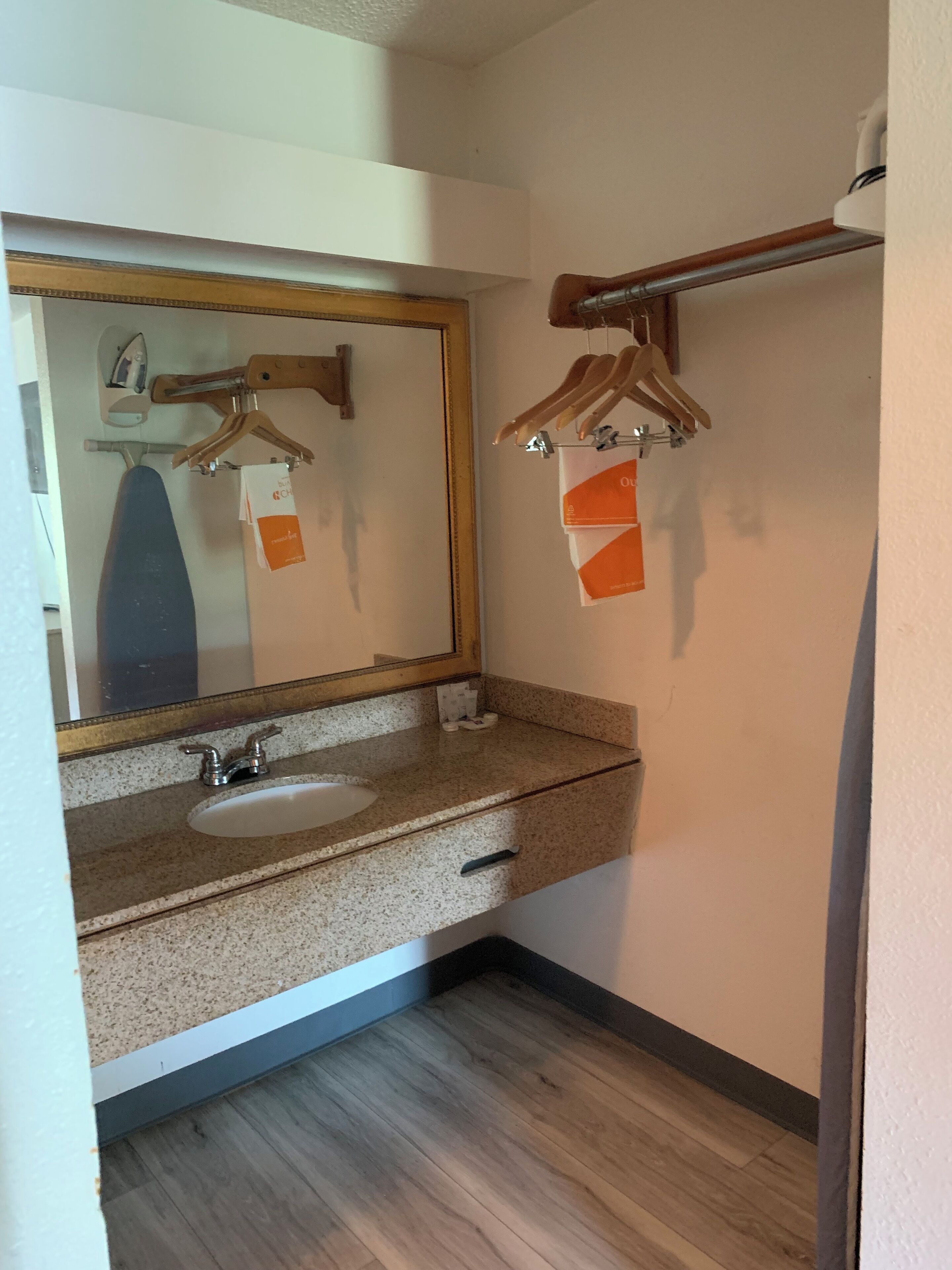 Un baño con encimera de granito, lavamanos blanco, espejo con marco de madera y toalleros de madera.