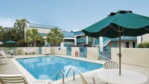 Une piscine entourée de chaises longues et de parasols, le tout bordé par un bâtiment doté d’un toit bleu.