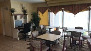 Une chambre d’hôtel comprenant un coin repas, un bureau avec un ordinateur et une grande fenêtre avec des rideaux.