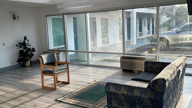 Une pièce spacieuse avec un plafond haut, de grandes fenêtres, un plancher en bois, un canapé bleu à motifs, une chaise en bois et un petit tapis.
