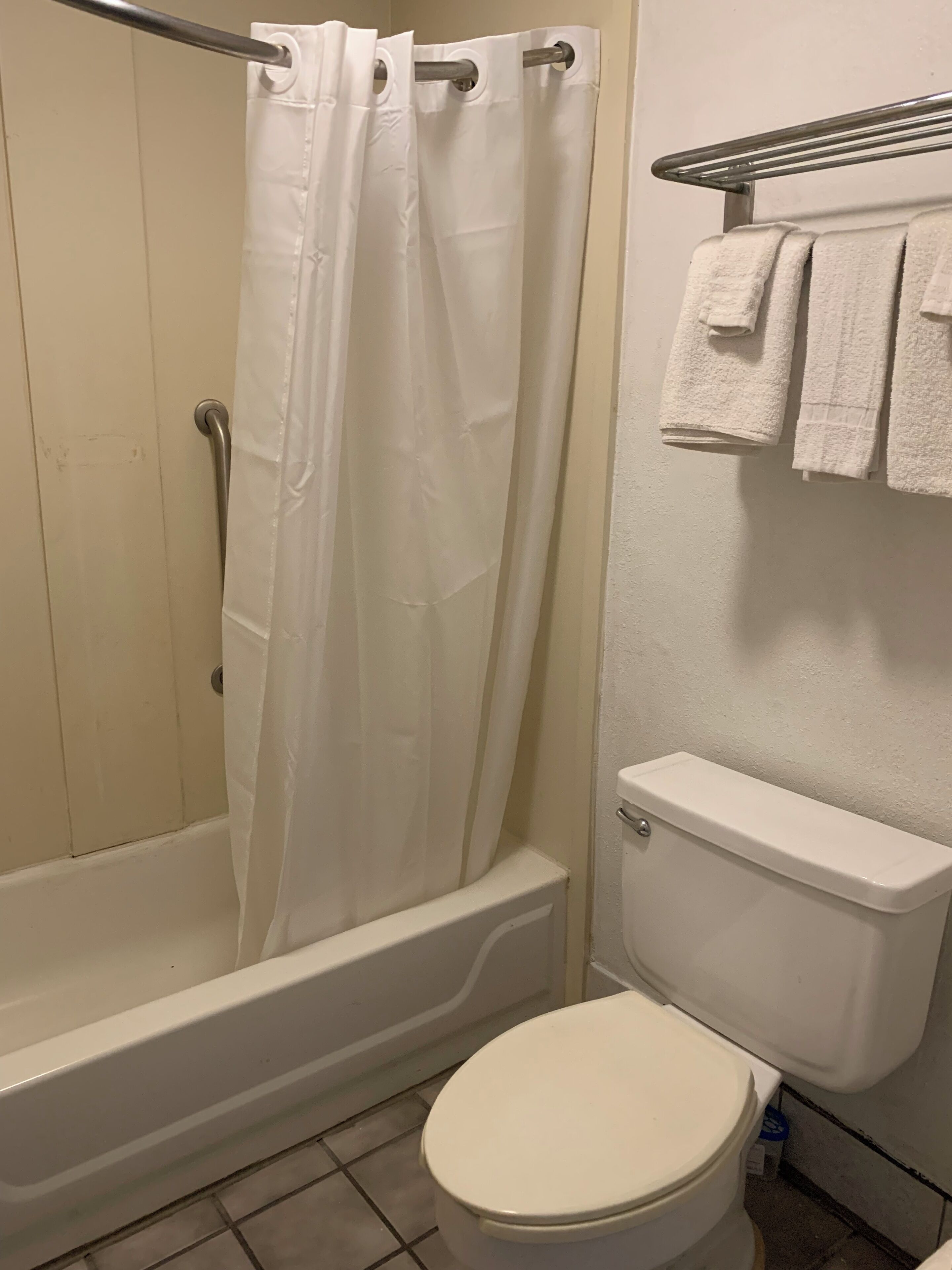 A bathroom with a shower curtain, a bathtub, a toilet, and a towel rack with towels.