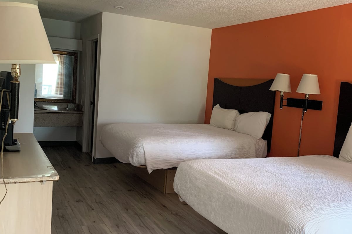 A hotel room with two beds, a desk, and a mirror.
