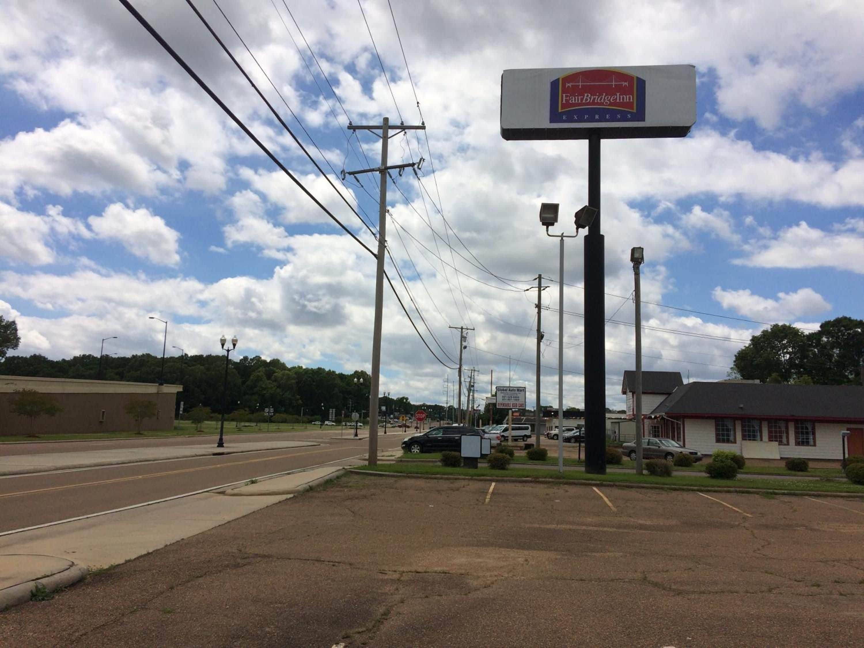 A parking lot with a FairBridge Inn Express sign, a Global Auto Mart sign, and a building with a red roof.