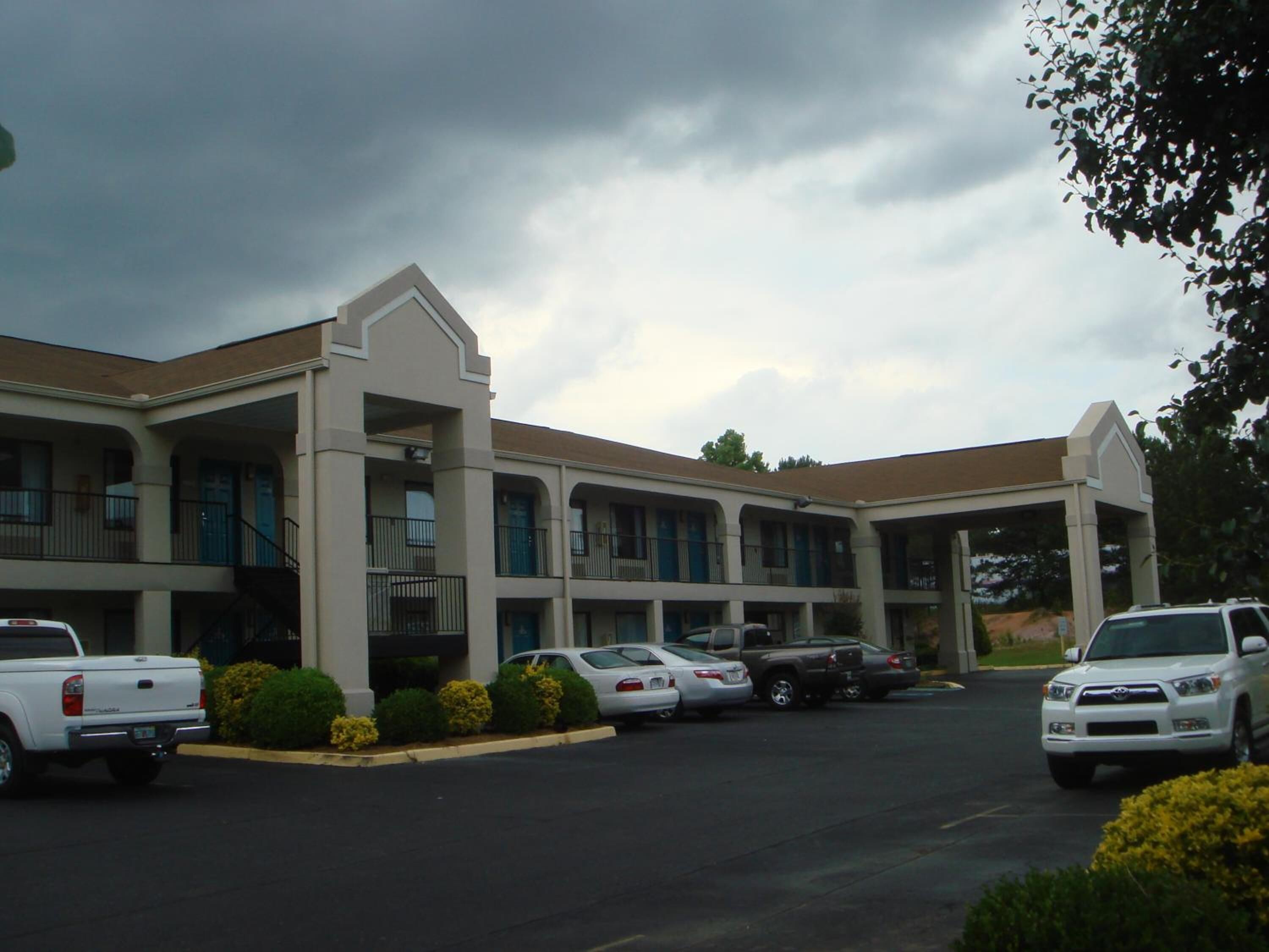 A motel with a central courtyard, multiple balconies, and a parking lot with several vehicles.