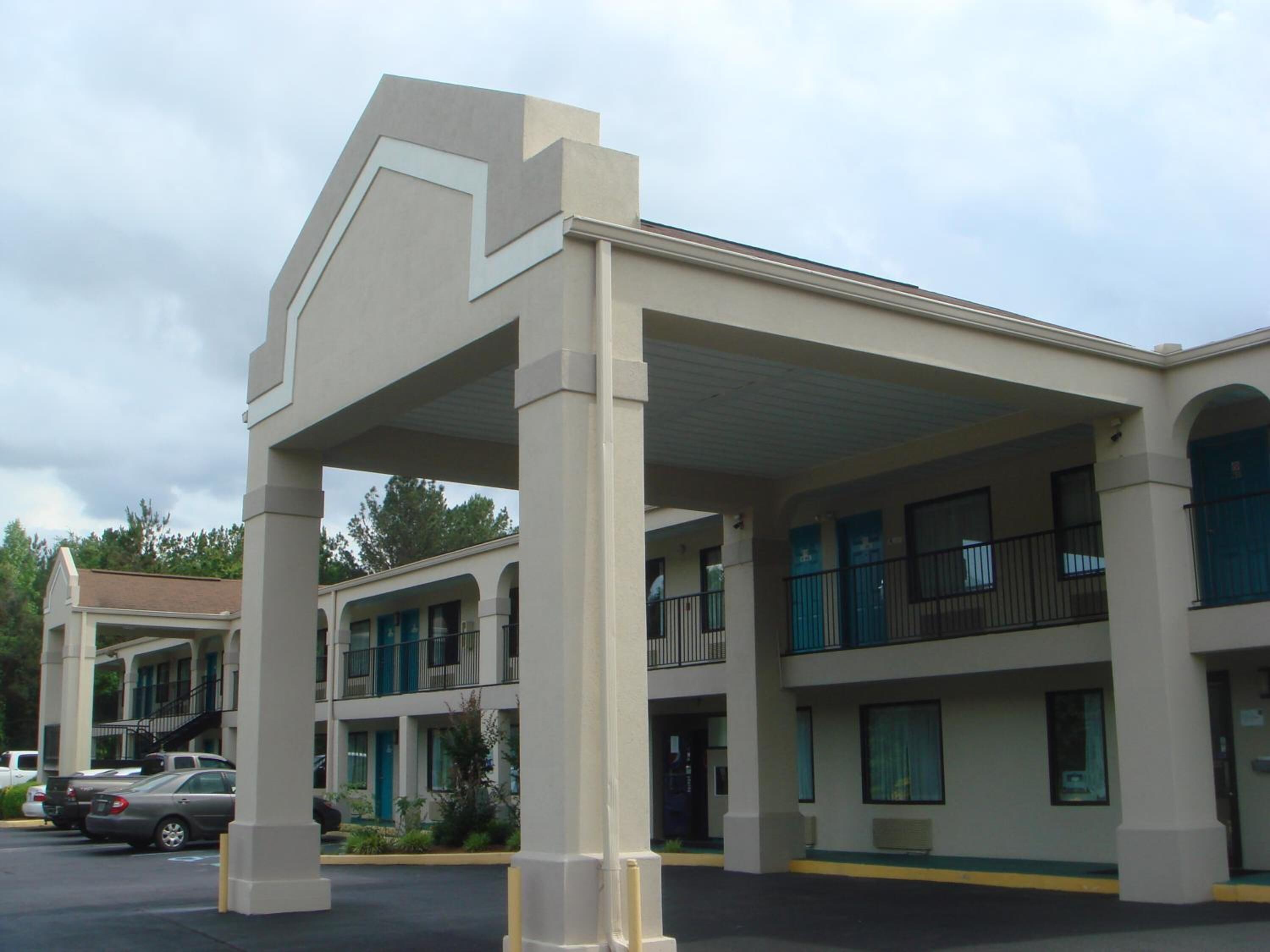 A motel with a central atrium, multiple balconies, and a parking lot with cars.